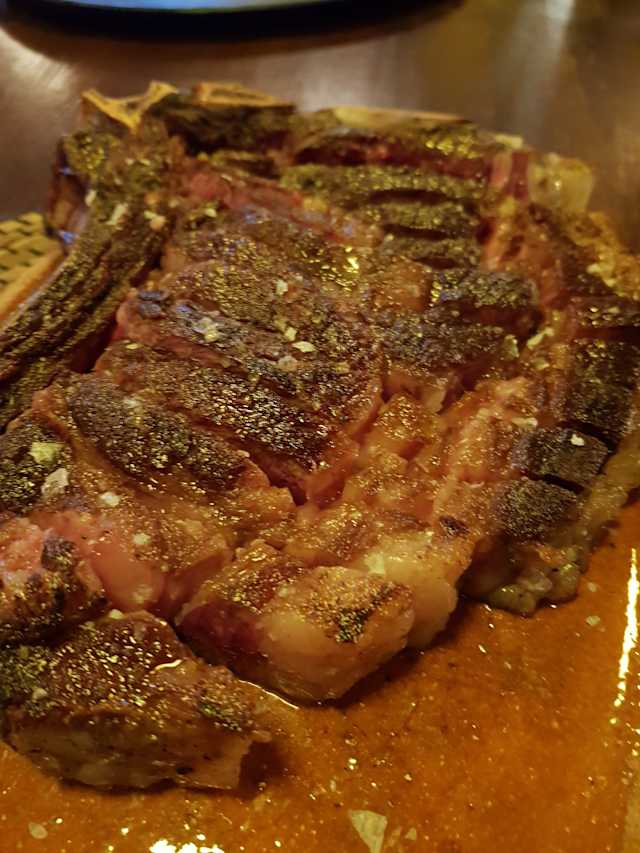 Un jugoso ribeye con una costra caramelizada y sazonada, que destaca por su tamaño generoso y su veteado, prometiendo una experiencia sabrosa.
