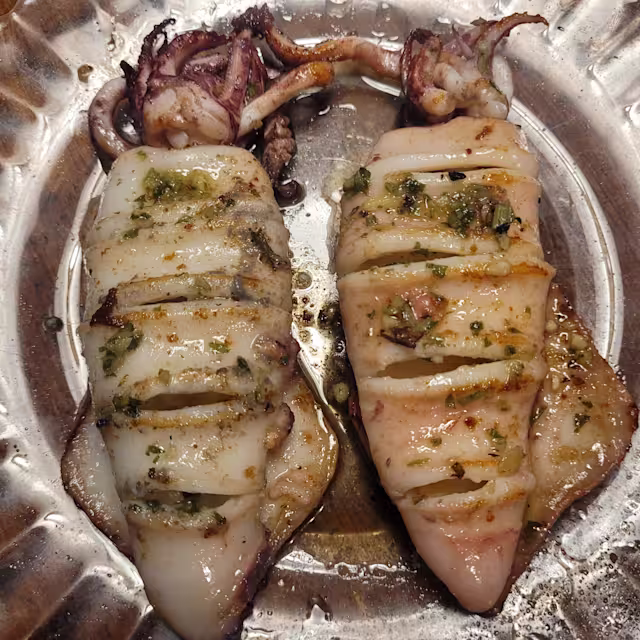 Calamares a la parrilla, uno entero y otro en rodajas, con salsa de hierbas frescas.