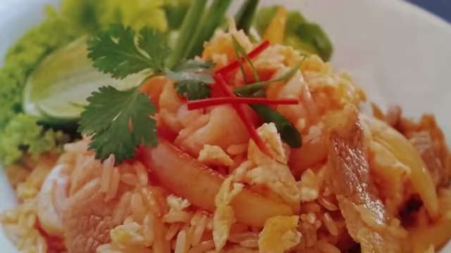 Arroz frito con camarones y huevo, adornado con cilantro fresco y rodajas de chile rojo, acompañado de limones y lechuga crujiente.