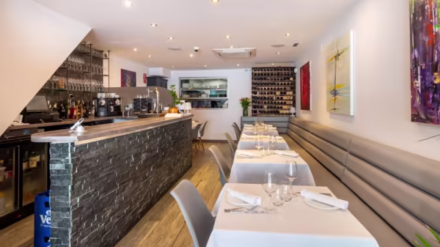 Interior moderno y elegante con elementos claros y oscuros, bancos tapizados grises, mesas simples y arte en las paredes, creando un ambiente acogedor y relajado.