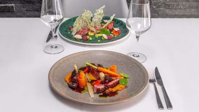 Carne estofada tierna acompañada de puré de zanahoria y verduras frescas, presentada de manera elegante con salsas contrastantes.