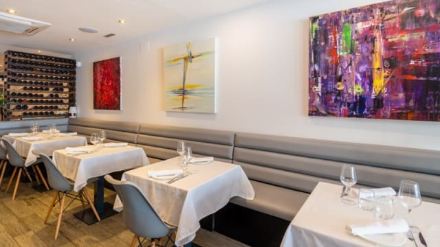 Interior de restaurante moderno y minimalista, con bancos tapizados en gris, manteles blancos y arte abstracto en las paredes.