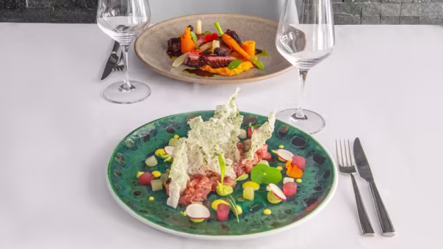 Plato colorido con carne picada, espuma de hierbas verdes y elementos crujientes, acompañado de un segundo plato de verduras asadas y carne tierna.