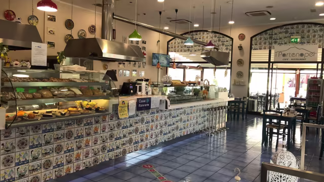 Interno di un ristorante con un bancone espositivo di prodotti da forno, tra cui dolci e pane, e un'atmosfera accogliente e informale.