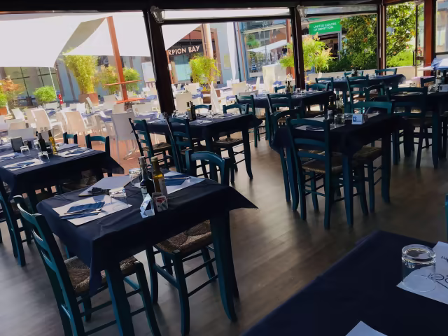 Interno di un ristorante spazioso con tavoli ordinati, tovaglie blu scuro e sedie blu, che creano un'atmosfera accogliente e informale.