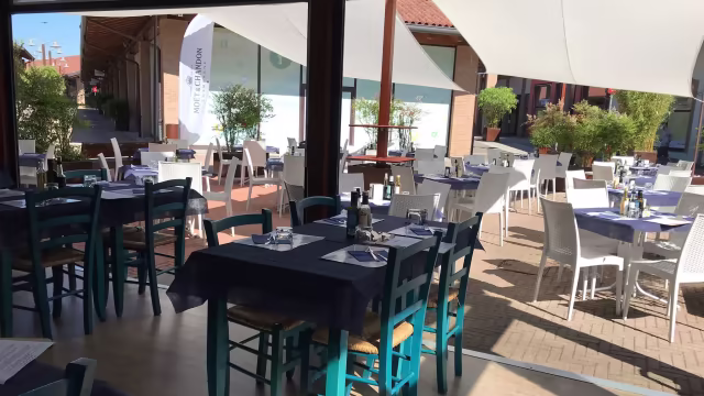 Interno di ristorante luminoso e arioso, con tavoli in legno e sedie colorate, predominanti blu e bianche, pronto per gli ospiti.