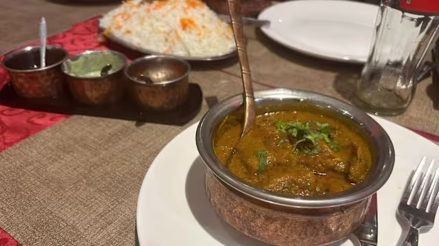 Plat de curry aromatique avec des morceaux tendres de viande ou de légumes dans une sauce épaisse et épicée, garni d'herbes vertes finement hachées, accompagné de riz blanc moelleux et de petits bols de condiments.