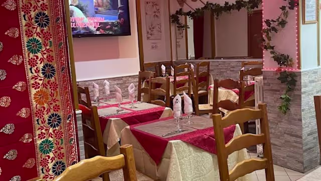 Intérieur de restaurant chaleureux avec des chaises et tables en bois, nappes élégantes rouges et crème, murs décorés et ambiance accueillante.