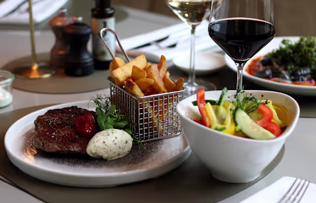 Saftig gegrilltes Steak, serviert mit knusprigen Pommes frites, Kräuterbutter und einem frischen Salat aus buntem Gemüse.