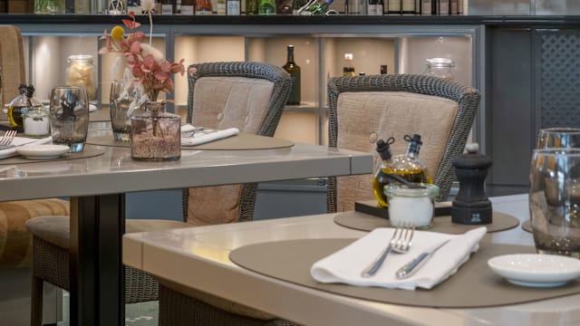Modernes Restaurantinterieur mit eleganter Einrichtung, gepolsterten Stühlen, sanfter Beleuchtung und dekorativen Blumenelementen für eine einladende Atmosphäre.