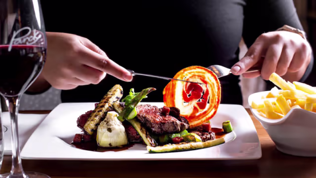 Perfect gebakken stuk vlees, waarschijnlijk steak, geserveerd met gegrilde groenten zoals asperges en courgette, een geroosterde tomaat bovenop en krokante frietjes aan de zijkant.