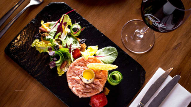 Zalm tartaar mooi gepresenteerd in een ronde vorm, getopt met een kwartelei, omringd door frisse groenten zoals sla en microgroenten, met komkommer spiralen en tomatenblokjes voor kleur.