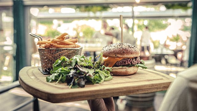 Hamburger juteux avec un épais steak de boeuf, fromage fondu et pain moelleux aux graines de sésame, accompagné de frites croustillantes et d'une salade de jeunes pousses.