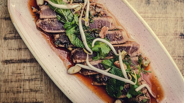 Plat élégamment présenté avec des tranches de thon grillé, accompagné d'une sauce savoureuse et garni d'herbes fraîches, d'ail émincé et de jeunes pousses.