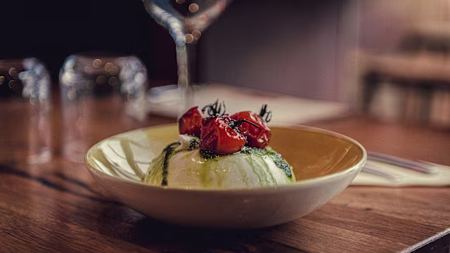 Plat crémeux de burrata, garni de tomates cerises rôties légèrement caramélisées, arrosé d'huile d'herbes vertes et décoré de jeunes herbes fraîches.