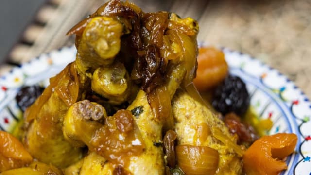 Poulet tendre braisé dans une sauce riche et épicée, accompagné de fruits secs comme des abricots et des pruneaux, et garni d'oignons caramélisés.