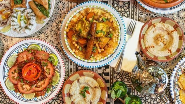 Variété de plats marocains, avec un couscous coloré garni de légumes, accompagné de salades fraîches, de pâtisseries dorées, de houmous crémeux et de riz bien assaisonné.