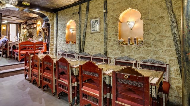 Intérieur de restaurant chaleureux avec des chaises en bois ornées de rembourrage rouge, murs en pierre naturelle et éclairage doux, créant une ambiance conviviale.