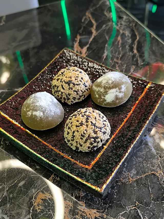 Assiette composée de quatre desserts ronds, deux saupoudrés de sucre glace et deux recouverts de graines de sésame, avec une apparence brillante et une texture moelleuse.
