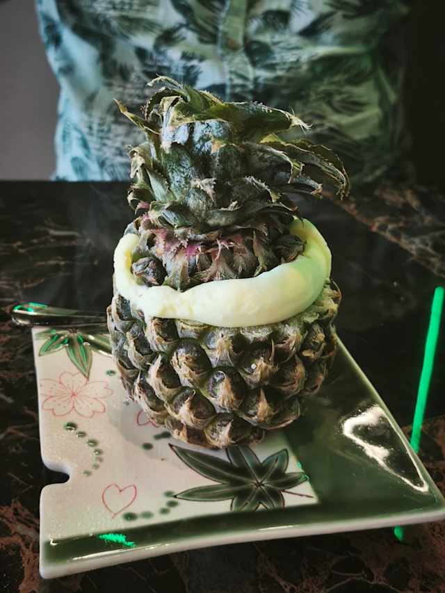 Plat créatif avec une ananas évidé rempli d'une préparation légère et crémeuse, probablement un dessert ou une salade de fruits, conservant son sommet pour une touche ludique.
